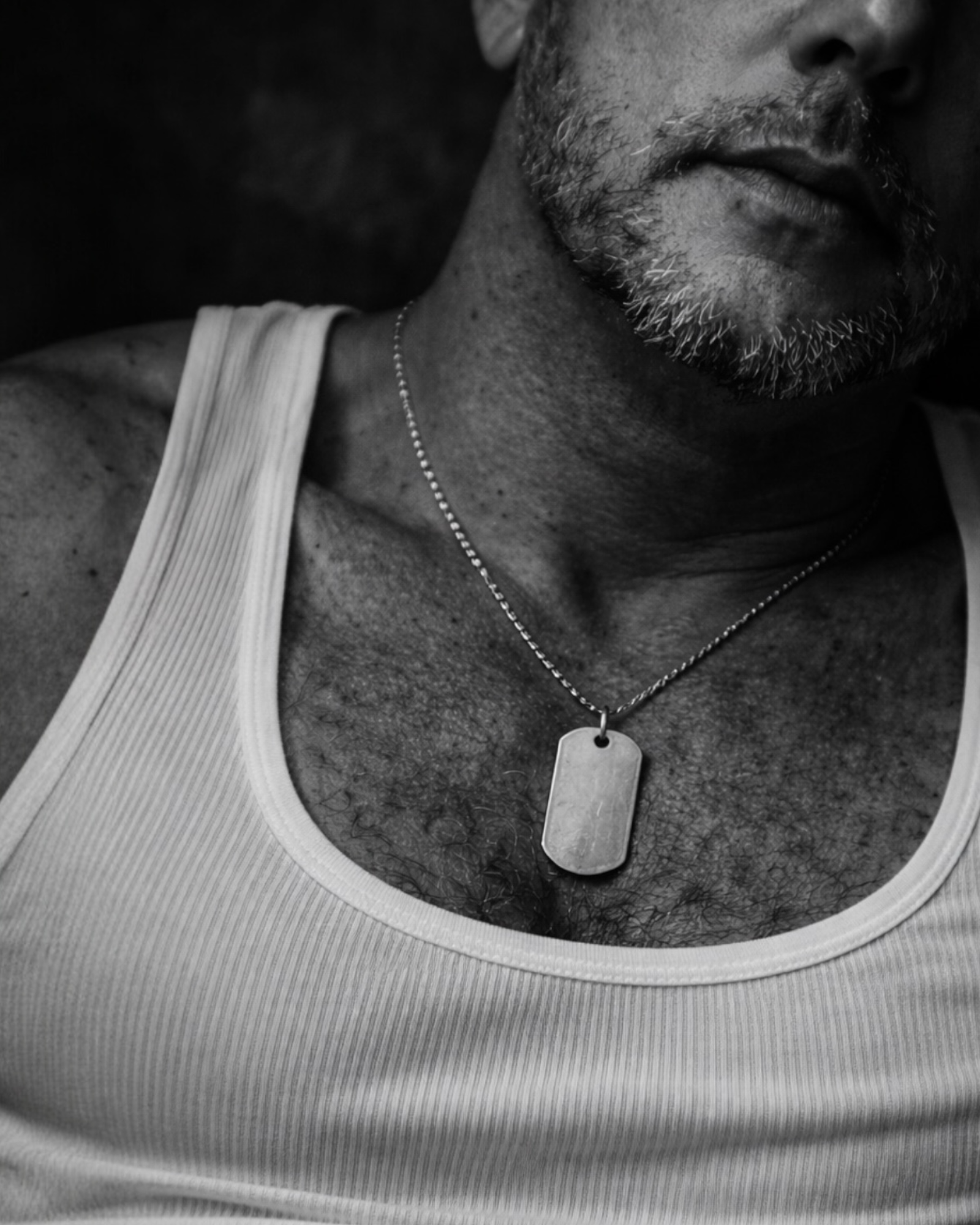 Black and white close-up of man wearing sterling silver dog tag necklace on chest, minimalist and symbolic MARKED jewellery