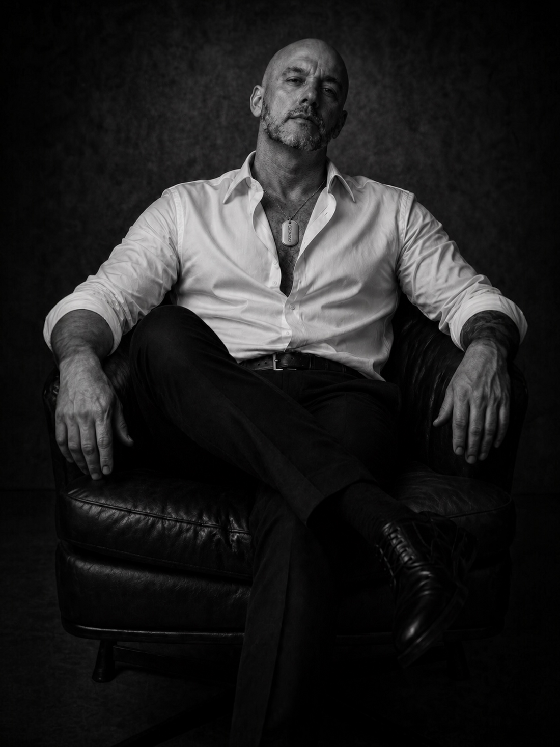 Black and white portrait of a man in an open white shirt wearing a sterling silver MARKED dog tag, expressing calm confidence, honesty and quiet self-possession.