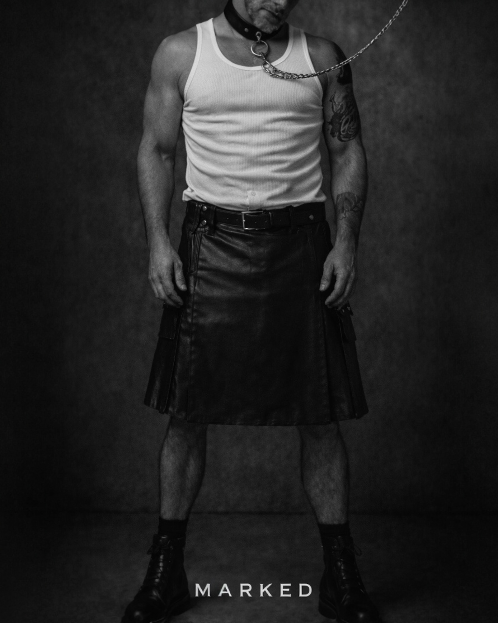 Black and white portrait of man wearing leather kilt and chain collar necklace, MARKED SURRENDER collection, masculine silver jewellery aesthetic