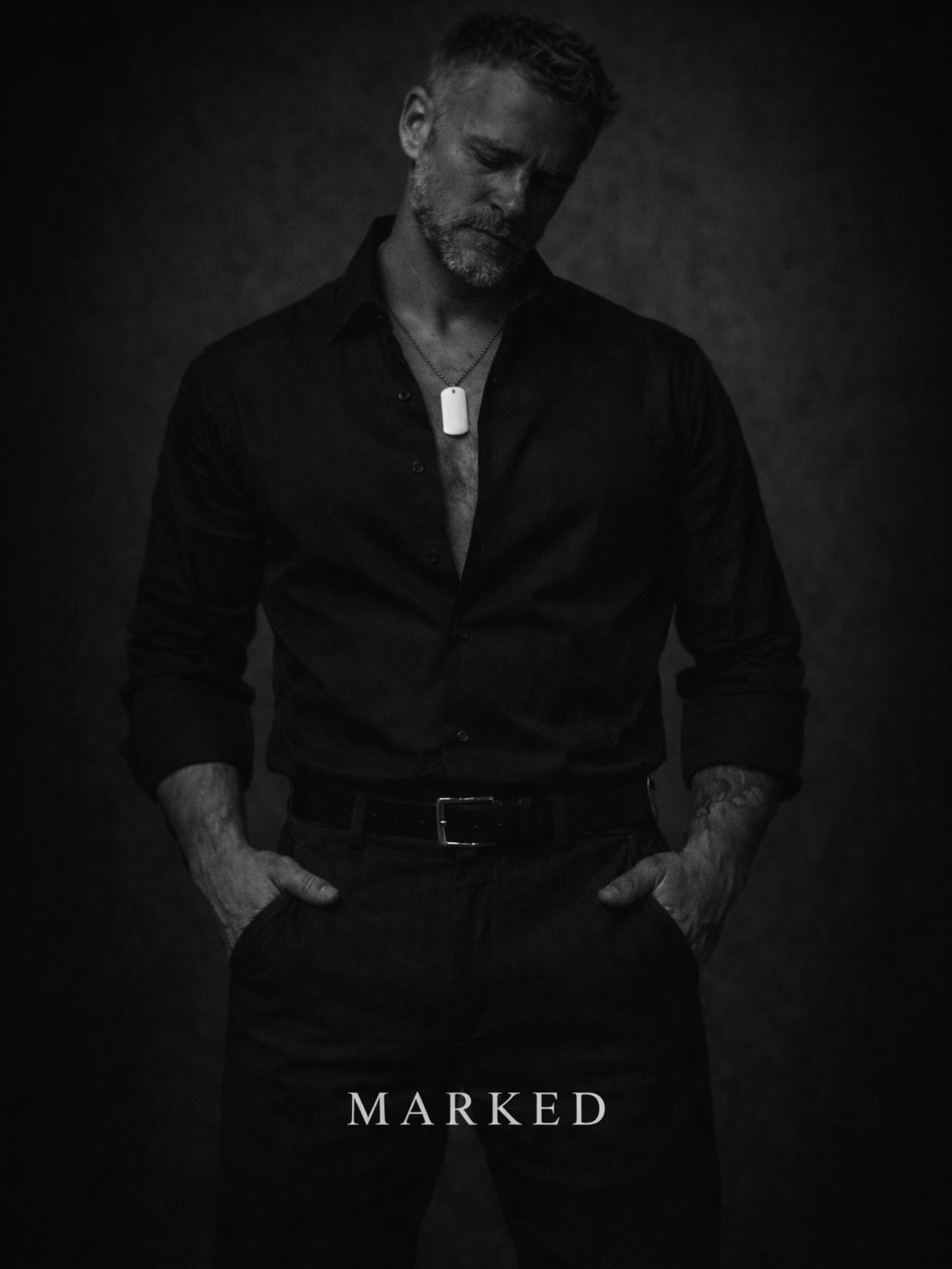Well-dressed man in black shirt wearing a dog tag necklace, black and white portrait conveying controlled masculinity and refined dominance – MARKED jewellery